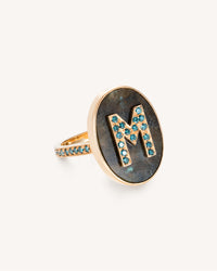 18K Yellow gold initial ring, with table of Labradorite stone and initial with blue diamond pavé stones on white background