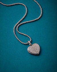 close up of 18k white 40 cm discoball necklace connected with small 18k white gold diamond pavé cuore pendant on turquoise background